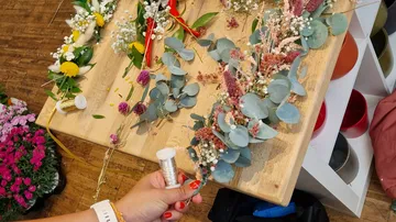 Hand fertigt Blumenkränze auf einem Holztisch.