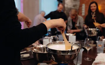 Person stirring cheese fondue at a gathering.