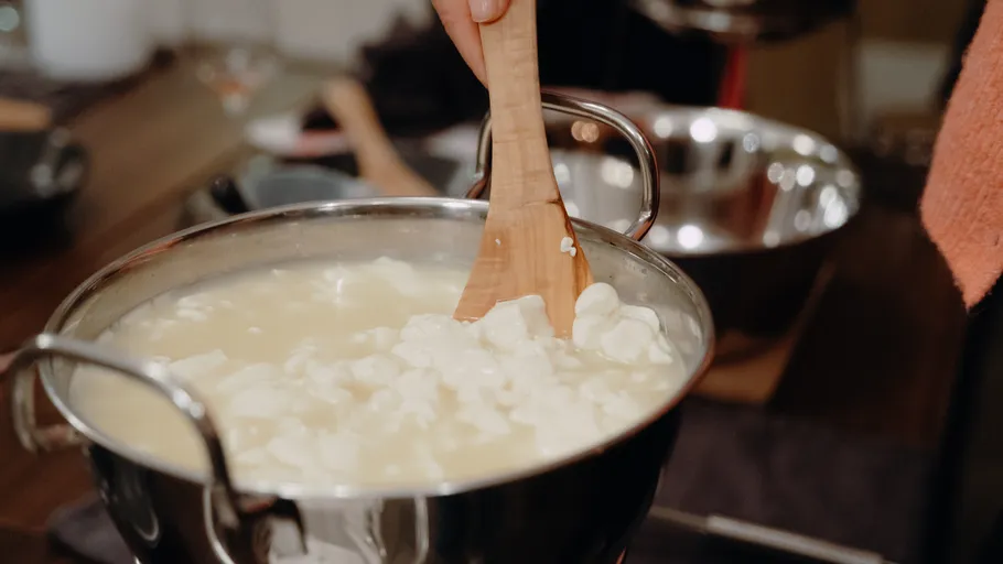 Hand stirring curds in a pot, kitchen scene.