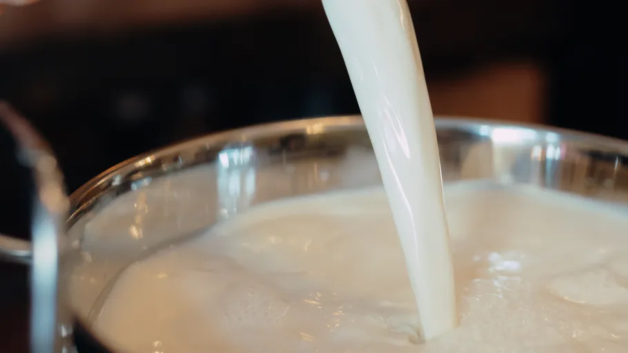 Milch wird in einen Metalltopf gegossen.