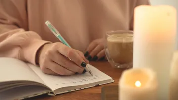 Person schreibt im Notizbuch neben Kerzen.