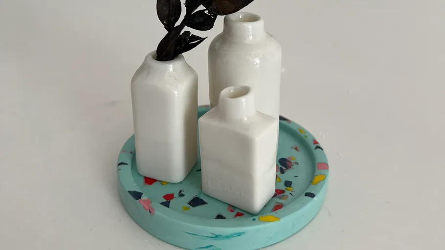 Three white vases on colorful round tray.