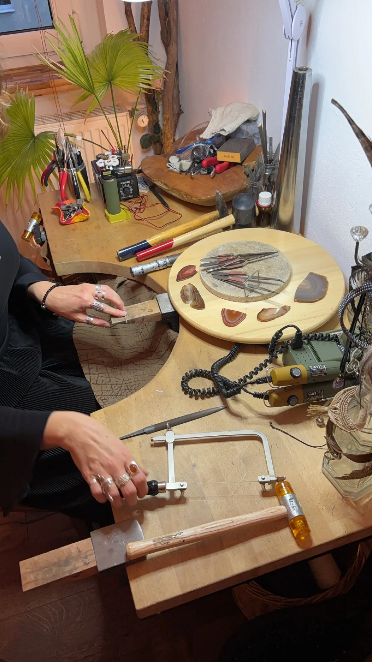 Person fertigt Schmuck an unordentlichem Arbeitstisch.