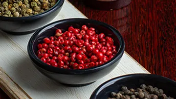Bowls of different peppercorns on wooden board.