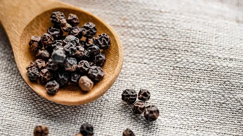 Black peppercorns on wooden spoon, fabric background.