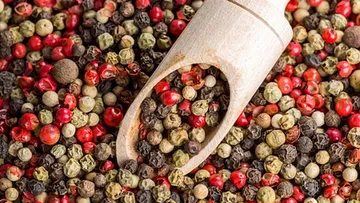 Mixed peppercorns with a wooden scoop.
