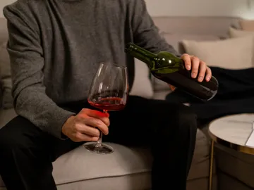 Eine Person gießt Rotwein in ein Glas auf einem Sofa.
