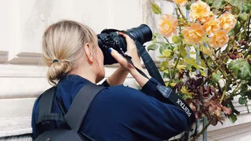 Person photographing flowers on a wall.