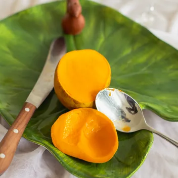 Cut mango with knife and spoon, green plate.