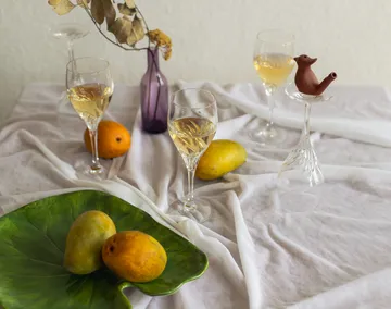 Glasses, mangoes, vase on white tablecloth.