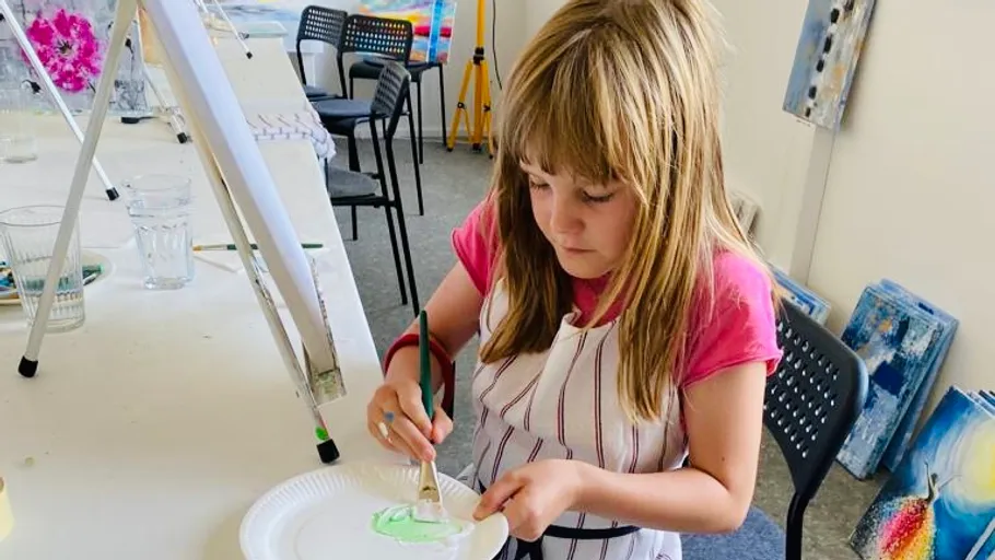 Girl painting on paper plate in art studio.