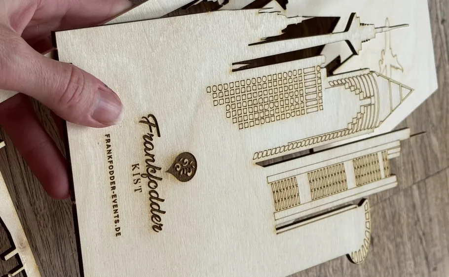 Hand hält Holz-Laserschnitt mit Skyline-Design.