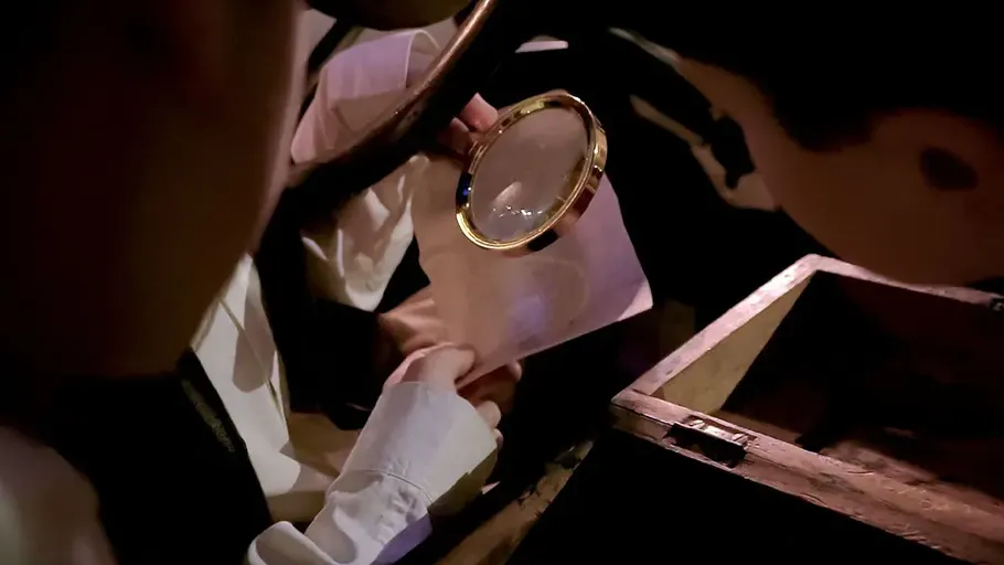 Person examining envelope with magnifying glass indoors.