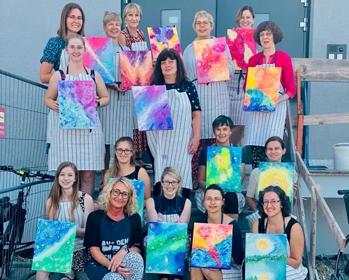 Group of women holding colorful paintings outdoors.