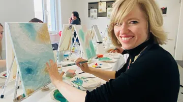 Woman painting canvas in art class setting.