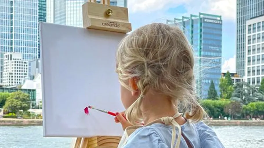 Child painting outdoors with city skyline background.