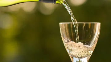 White wine pouring into glass, outdoor setting.