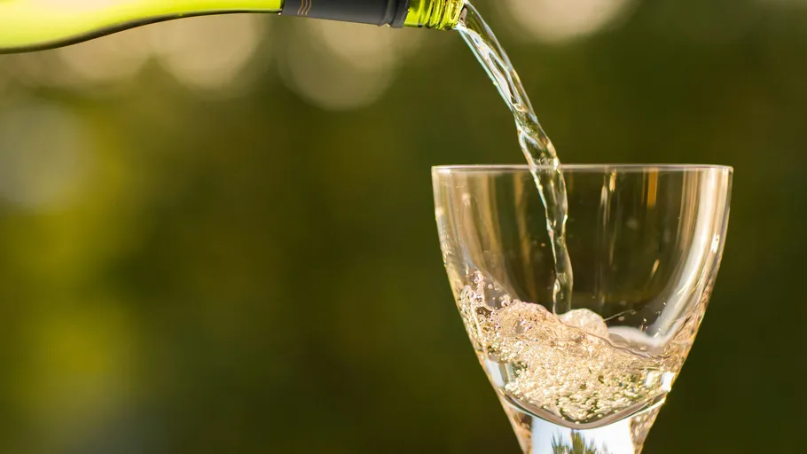 Weißwein wird in Glas im Freien gegossen.