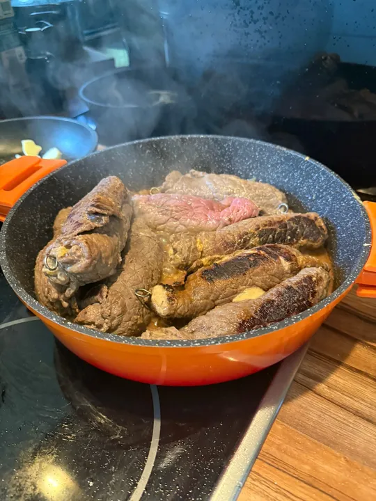 Beef roulades cooking in a pan.