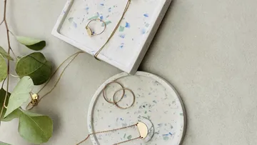 Goldschmuck auf Terrazzo-Tabletts mit Blättern.