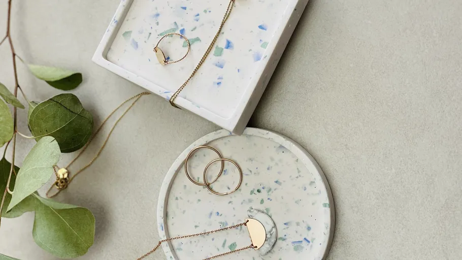 Goldschmuck auf Terrazzo-Tabletts mit Blättern.