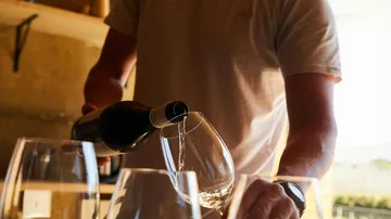 Person gießt Wein in Gläser drinnen.