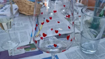 Glass with red hearts on newspaper-covered table.