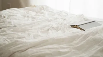 Book resting on rumpled white bedspread.