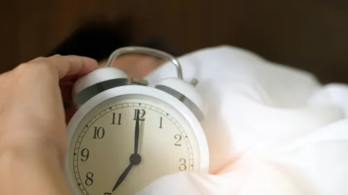 Hand reaching alarm clock, morning bed.