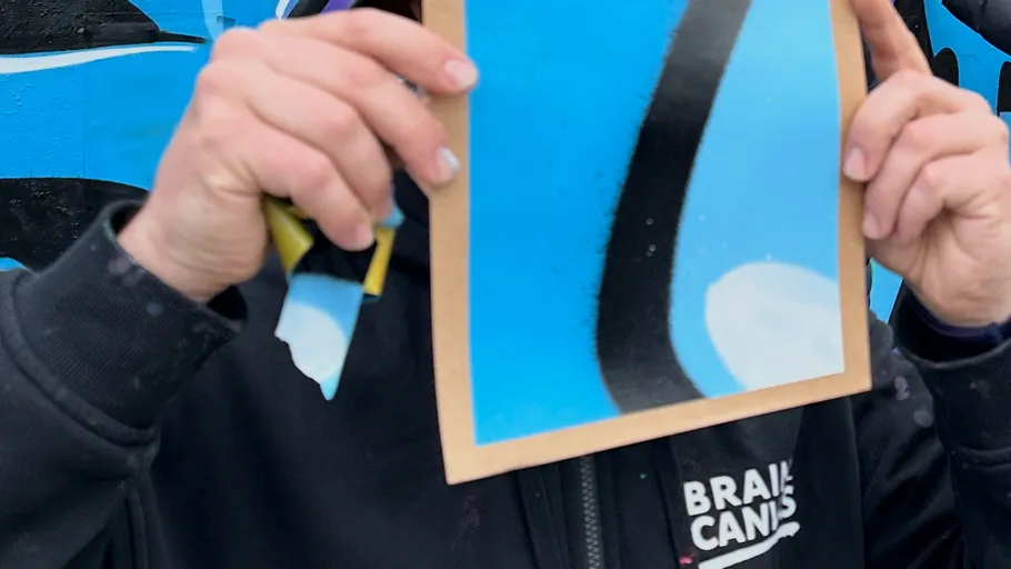 Person hält bemalte Tafel, bunter Wandhintergrund.