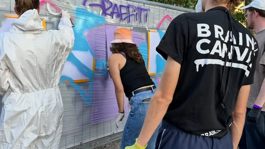 People spray paint graffiti on a wall.