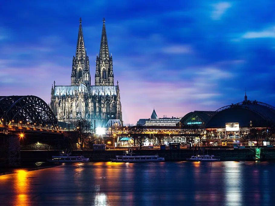 Kölner Dom reflektiert im Wasser, umgeben von Stadtlichtern.