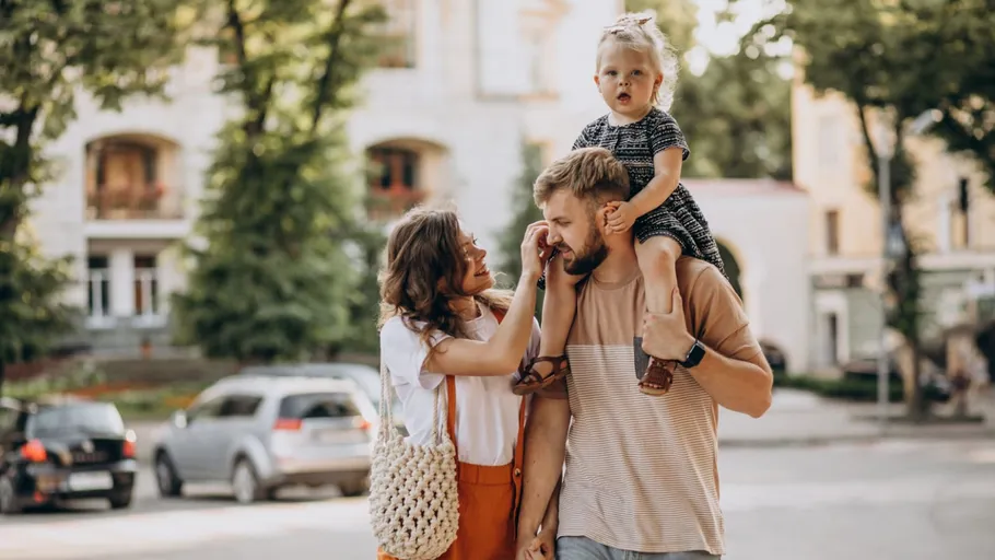 Family walking outdoors, child on father's shoulders.