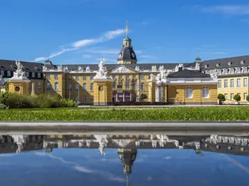 Historic building is reflected in water under a blue sky.
