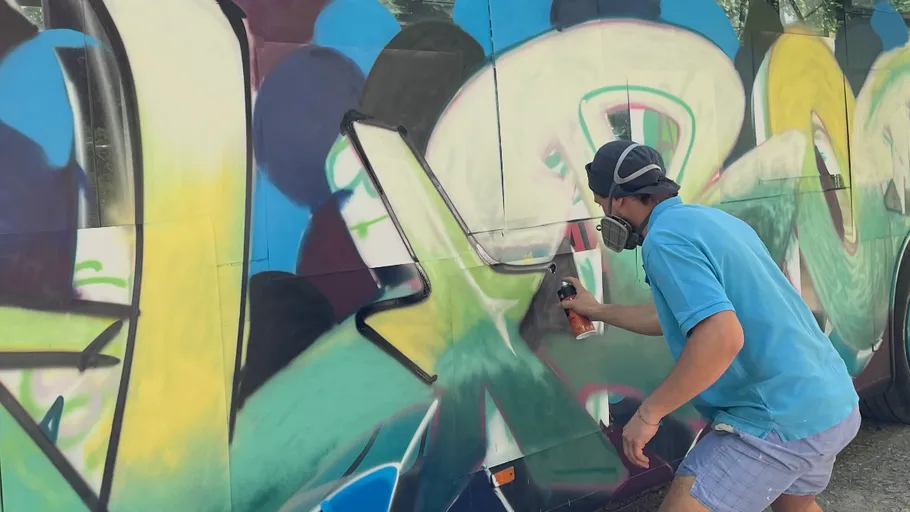 Person sprüht buntes Graffiti auf eine Wand.