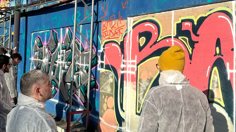Personen in Schutzanzügen betrachten Graffiti-Kunst.