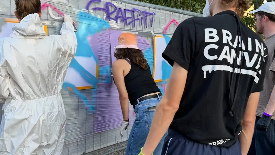 Personen malen Graffiti an eine Wand im Freien.