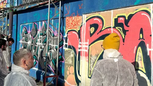 Menschen in Schutzanzügen betrachten Graffiti-Wand.