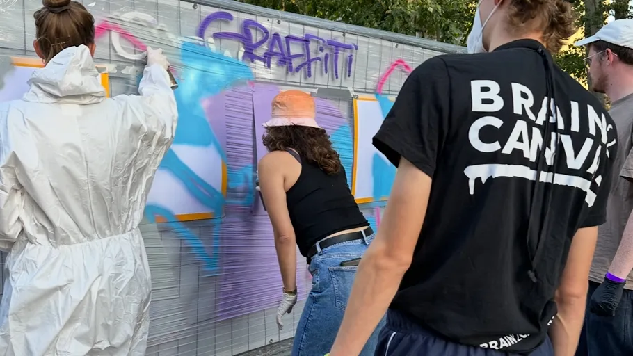 Menschen sprühen Graffiti auf eine Wand im Freien.