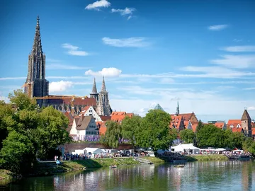City view with church, people by the river, sunny sky.