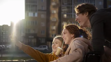 Three friends taking selfie outdoors, smiling.