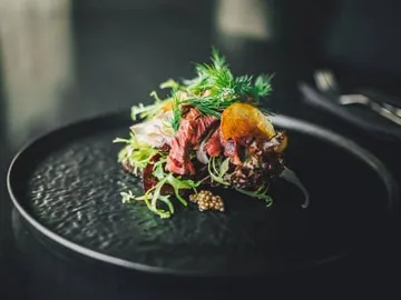 A dish with meat and fresh herbs on a black plate.