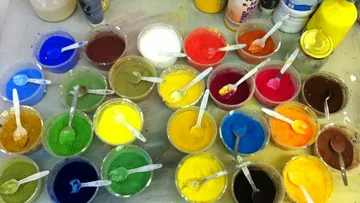 Bunte Pigmente in Plastikbechern auf Tisch.