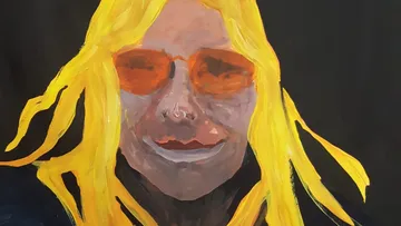 Person mit gelbem Haar, orange Brille, dunkler Hintergrund.