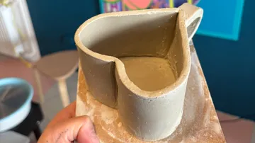 Hand hält einen herzförmigen Tonbecher drinnen.