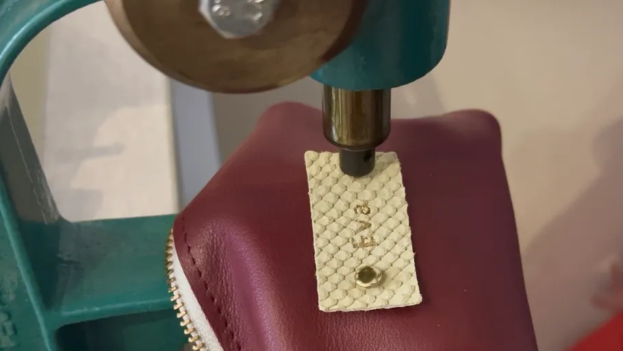 Embossing machine pressing leather tag on pouch.