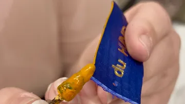 Hände halten eine blaue Karte mit gelbem Text.