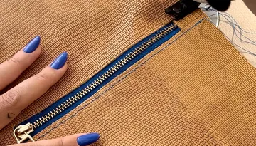 Person with blue nails holds brown textured bag.