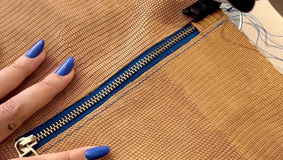 Person with blue nails holds brown textured bag.