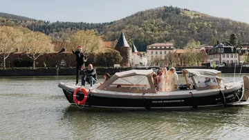 Boat with people on river, trees in background.